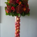 Tall autumnal vase filled with apples and decked with red hydrangeas, red roses and two toned ‘Cherry Brandy’ roses.