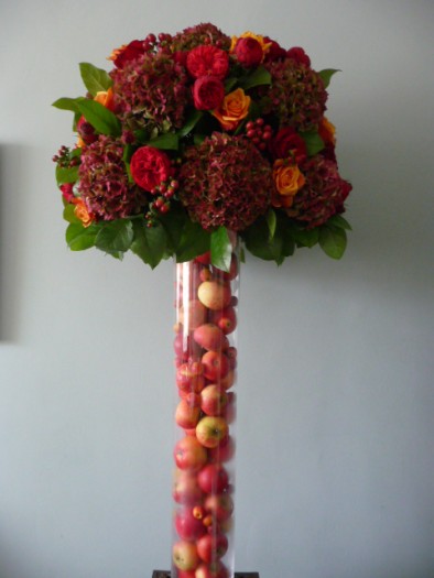 Tall autumnal vase filled with apples and decked with red hydrangeas, red roses and two toned ‘Cherry Brandy’ roses.