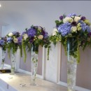 Tall vases of blue hydrangeas, purple eustoma, green spray roses and large headed cream roses