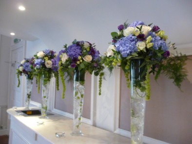 Tall vases of blue hydrangeas, purple eustoma, green spray roses and large headed cream roses